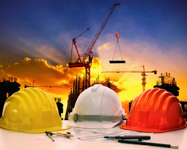 کلاه ایمنی روی میز کار مهندس عمران در برابر مواد بالابر جرثقیل در محل ساخت و ساز ساختمان