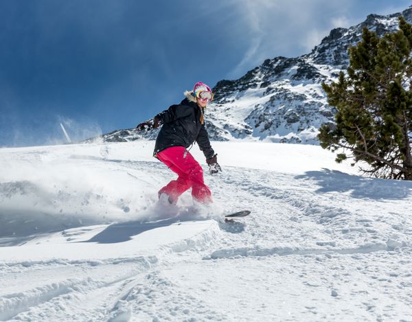 زن جوان اسنوبورد سوار در حال حرکت روی اسنوبرد در کوهستان
