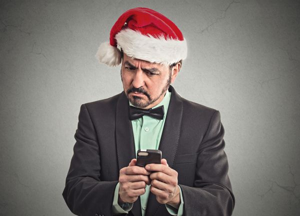 پرتره مرد بازرگان بامزه شکاک را که کلاه بابا نوئل قرمز بر سر دارد شگفت زده کرد و به معامله آنلاین معتبر گوشی های هوشمند نگاه می کند تا درست باشد احساسات بیان صورت زبان بدن فصل تعطیلی