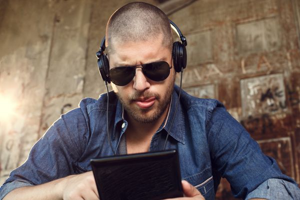 مرد جوان خوش تیپ در حال گوش دادن به موسیقی با هدفون از طریق رایانه لوحی