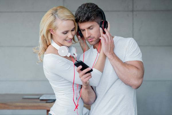 زوج جوان شیرین نیم تنه با لباس سفید در حال گوش دادن به موسیقی در تلفن