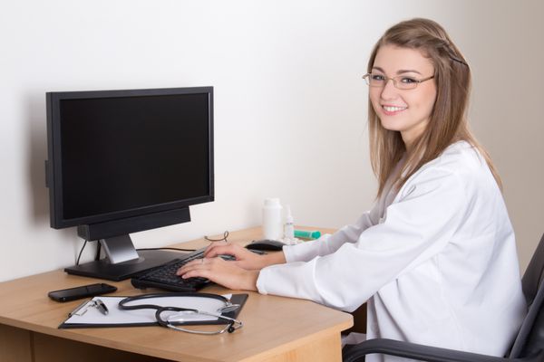 دکتر زن جوان شادی که با کامپیوتر در مطب کار می کند