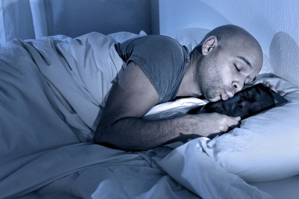 مرد جوان در رختخواب شب ها در حال خواب با تبلت دیجیتالی در حال بوسیدن صفحه لمسی روی دستگاه های اینترنتی و فن شبکه اجتماعی و مفهوم اعتیاد ارتباط آنلاین