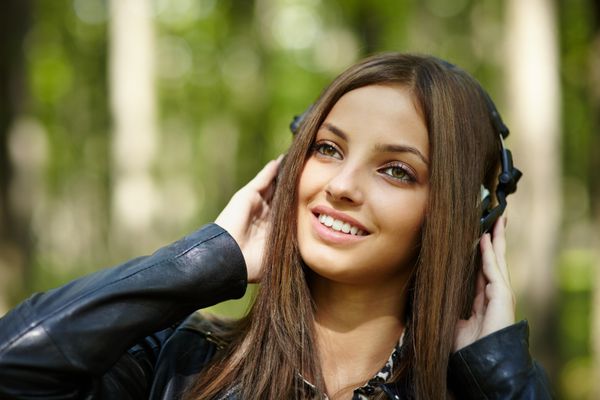 دختر نوجوان زیبا در حال گوش دادن به موسیقی با هدفون خود در فضای باز