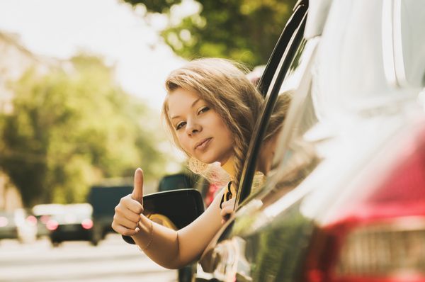 زن جوان زیبای قفقازی در ماشین که انگشت شست را نشان می دهد