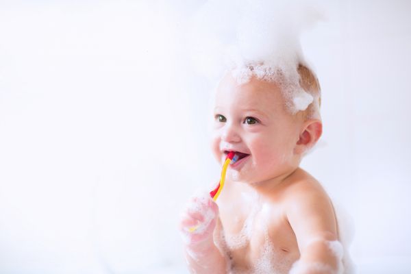 پسر بچه ی زیبا در حال حمام کردن با فوم و مسواک زدن دندان هایش در حمام آفتابی سفید