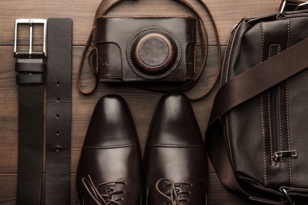 کفش قهوه ای کمربند کیف و دوربین فیلم روی میز چوبی