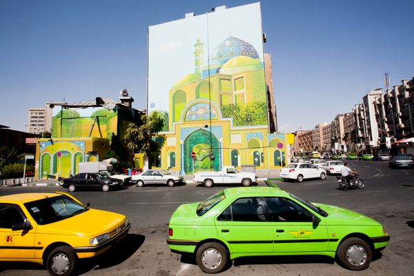 تهران ایران - 6 اکتبر ترافیک در جاده آفتابی با ماشین های تاکسی رنگارنگ و هنر خیابانی روی دیوار ساختمان در 6 اکتبر 2014 با جمعیت با 8 3 میلیون نفر تهران سی و دومین پایتخت ملی ایران است