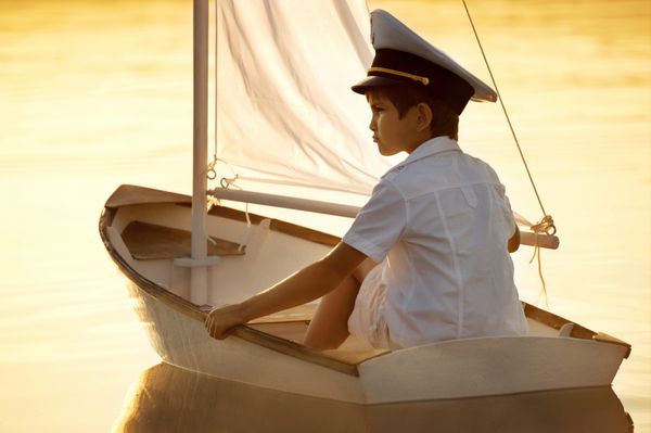 دریانورد پسر در غروب آفتاب در یک عصر گرم تابستان بر روی یک قایق بادبانی شناور است