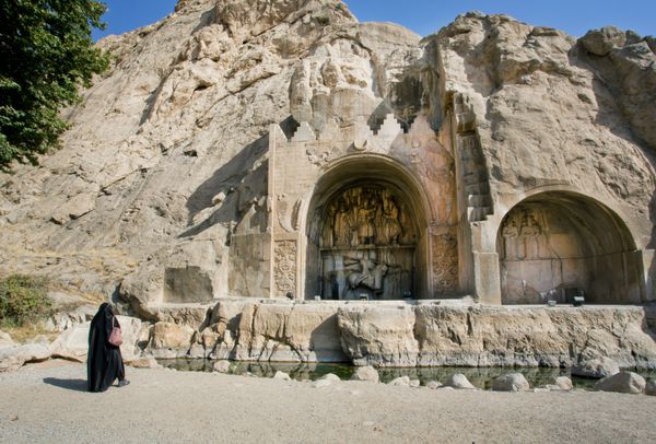کرمانشاه ایران - 12 اکتبر زن تنها با حجاب مسلمان در نزدیکی بنای تاریخی طاق بستان در 12 اکتبر 2014 ایستاده است طاق بستان نقش برجسته ای از قرن چهارم دوران امپراتوری ایران ساسانی است