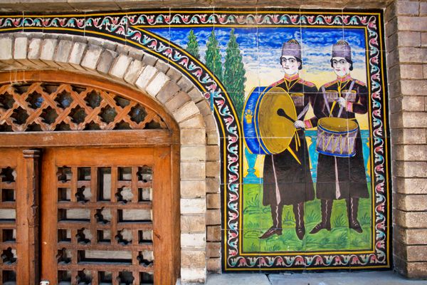 تهران ایران - 6 اکتبر دو نوازنده با دی‌اس با کاشی و سرامیک روی دیواری از گلستان قدیمی ایرانی در 6 اکتبر 2014 سایت میراث جهانی یونسکو گلستان دوست در قرن 16 ساخته شد