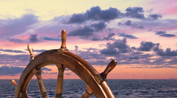 فرمان روی کشتی در پس زمینه غروب خورشید چرخ کاپیتان در یک کشتی قدیمی سکان کشتی روی قایق بادبانی نمای جانبی