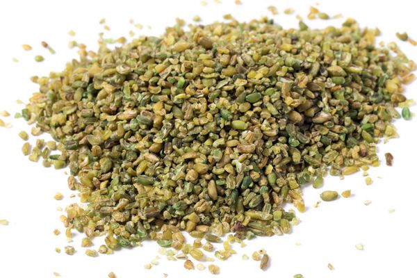 انبوهی از دانه های فریکه یا فریکه روی زمینه سفید غلات از گندم نارس و سبز رنگ تهیه می شود که در آتش برشته می شود تا یک غذای سالم و با شاخص گلیسمی پایین و سرشار از پروتئین و مواد معدنی باشد