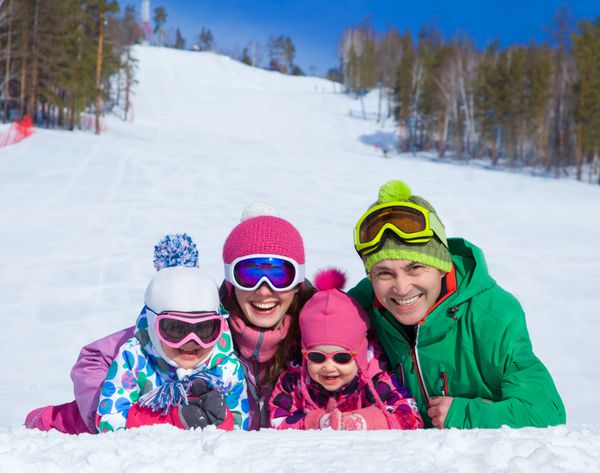 خانواده شاد با لباس زمستانی در پیست اسکی روی برف دراز می کشند