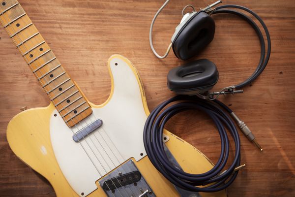 ضبط گیتار یک گیتار الکتریک و یک هدفون حرفه‌ای روی میز چوبی یا روستایی با نور گرم از نوع پنجره