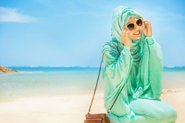دختر زیبایی با لباس سنتی مسلمان در ساحل نشسته است