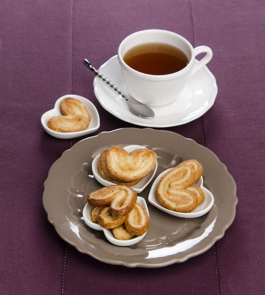 نخل های شیرینی شیرینی فرانسوی در قلب های نعلبکی روی ظرف چای بژ در پس زمینه