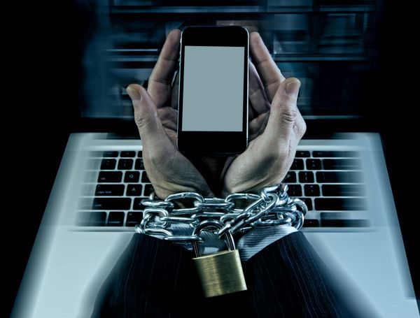 دست‌های یک تاجر قفقازی معتاد به تلفن همراه و قفل شده با مچ‌های زنجیر آهنی در اعتیاد به اینترنت گوشی‌های هوشمند و مفهوم معتاد به شبکه آنلاین