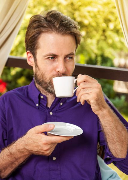 پرتره نزدیک مرد قفقازی چهل ساله در حال نوشیدن قهوه صبح در فضای باز در باغ ترر در طول روز آفتابی تابستان مفهوم آخر هفته یا تعطیلات حومه شهر