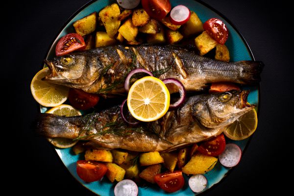 ماهی باس کبابی و سیب زمینی پخته در بشقاب تمرکز انتخابی