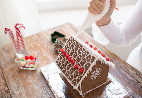 آشپزی مردم کریسمس و مفهوم دکوراسیون - نمای نزدیک از زن شاد که خانه های شیرینی زنجبیلی در خانه درست می کند