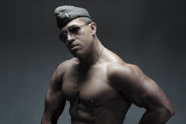 یک مرد جوان عضلانی در نور کم با کلاه نظامی و عینک آفتابی هوانوردی