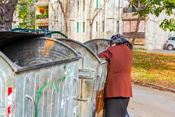 زن بی خانمان در زباله دان به دنبال غذا می گردد زن فقیر در حال جستجوی چیزی در ظرف است
