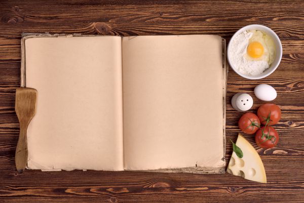 کتاب آشپزی قدیمی مواد لازم برای یک وعده غذایی روی پس‌زمینه‌ای از چوب قدیمی