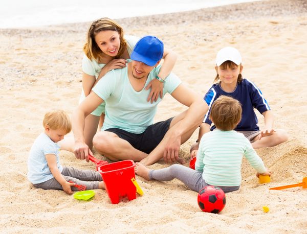 خانواده خندان با بچه هایی که در ساحل شنی استراحت می کنند