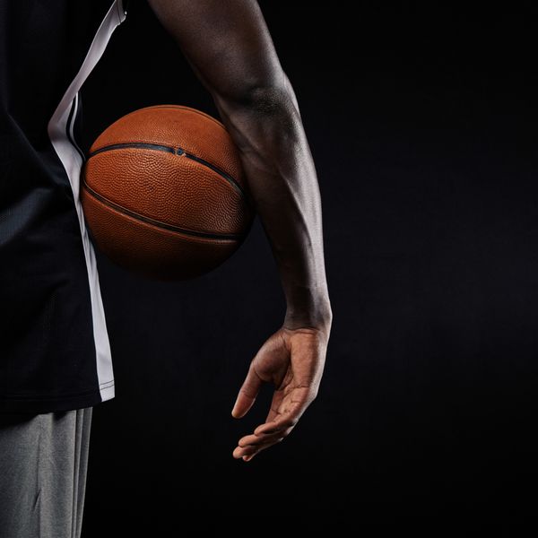 نمای نزدیک توپ بسکتبال در دست یک ورزشکار جوان آفریقایی در پس زمینه سیاه با کپی اسپ
