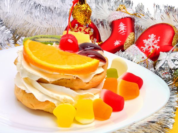 کیک میوه ای کریسمس با خامه روی بشقاب سفید و تزئین نقره ای رنگ