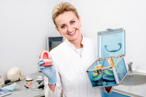 زن دندانپزشکی که فک های مصنوعی را در مطب دندانپزشکی نگه می دارد