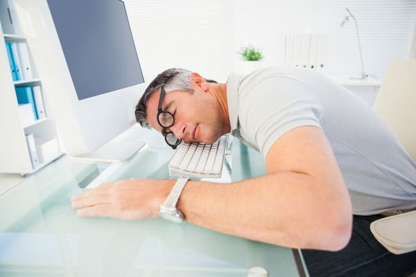 مردی با عینک که روی صفحه کلید پشت میز دفترش خوابیده است