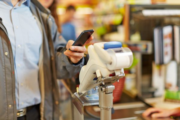 مردی در حال پرداخت بی سیم با گوشی هوشمند خود در صندوق سوپرمارکت