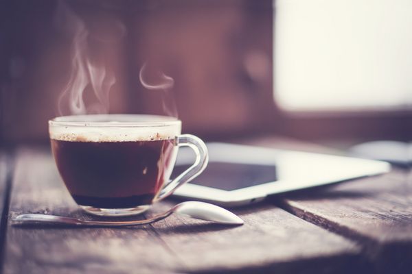 تبلت دیجیتال و فنجان قهوه روی میز چوبی قدیمی محل کار ساده یا استراحت قهوه با تمرکز انتخابی صبح