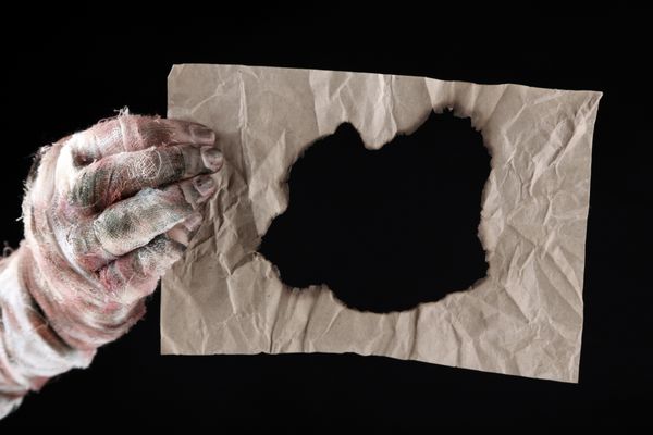 دست مومیایی که کاغذ قدیمی جدا شده روی سیاه را در دست گرفته است