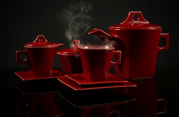 قهوه سرامیکی قرمز چای سرامیکی که روی پس‌زمینه بازتابنده سیاه با بخار ایستاده است