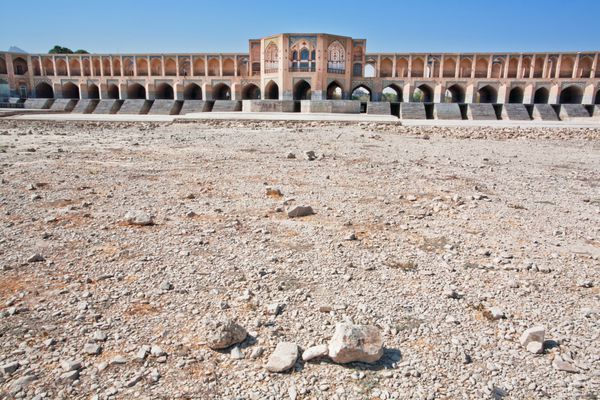 خاک خشک در بستر رودخانه ای خشک شده با پل قدیمی در پس زمینه اصفهان ایران خاور میانه