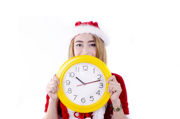 زن زیبا با لباس بابا نوئل که ساعت را روی پس زمینه سفید نشان می دهد