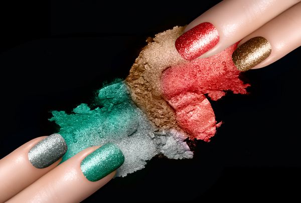 نمای نزدیک از دست‌های زنانه با ناخن‌های رنگ شده و نمونه‌های سایه چشم معدنی با رنگ‌های جشن در پس‌زمینه مشکی