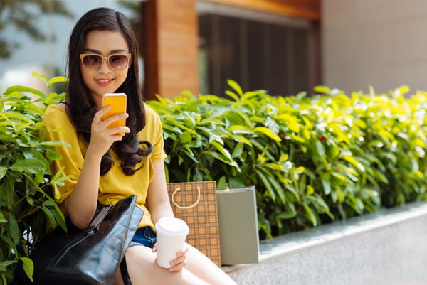 دختر نوجوان خندان با پیامک تلفنی در فضای باز