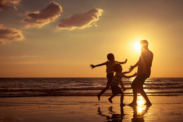 پدر و فرزندان در هنگام غروب آفتاب در ساحل مفهوم خانواده دوستانه