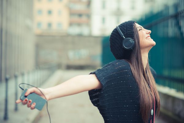 دختر جوان زیبا در حال گوش دادن به هدفون موسیقی در فضای باز