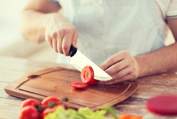 مفهوم آشپزی و خانه - نمای نزدیک گوجه فرنگی نر برش دستی روی تخته برش با چاقوی تیز