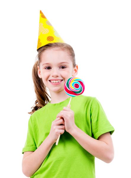 پرتره دختر کوچک خندان با تی شرت سبز و کلاه مهمانی با آب نبات رنگی - جدا شده روی سفید