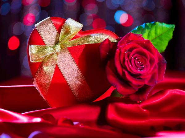 جعبه هدیه قلب قرمز و گل رز قرمز در پس زمینه ابریشم قرمز بر روی پس زمینه درخشان تعطیلات خیابان طراحی کارت روز عشق