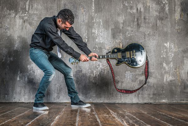 مردی در حال شکستن گیتار روی زمین