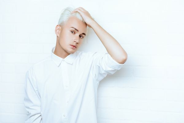 مرد جوان زیبا با نگاه حسی که در استودیو کنار دیوار آجری سفید ژست گرفته است مدل مو مد
