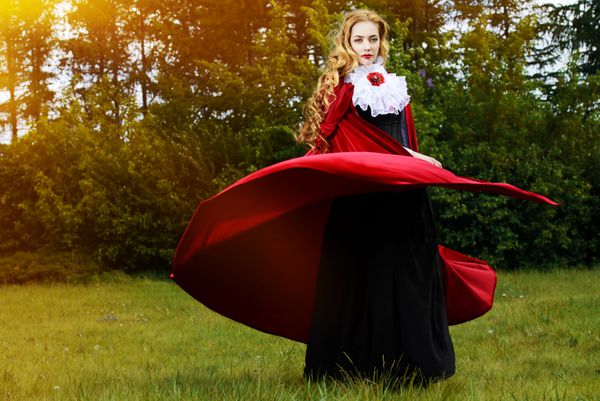 زن زیبا با لباس قدیمی و شنل قرمز در جنگل پری