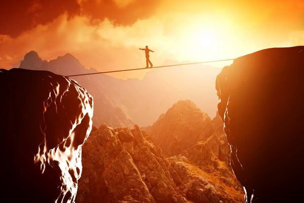 مردی که در هنگام غروب خورشید روی طناب بر فراز پرتگاه کوهستانی راه می‌رود و تعادل برقرار می‌کند مفهوم کسب و کار ریسک پذیری چالش تمرکز